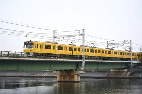 京急線の橋上を走るハッピーターントレイン——黄色いイエローハッピートレインをラッピングした車両